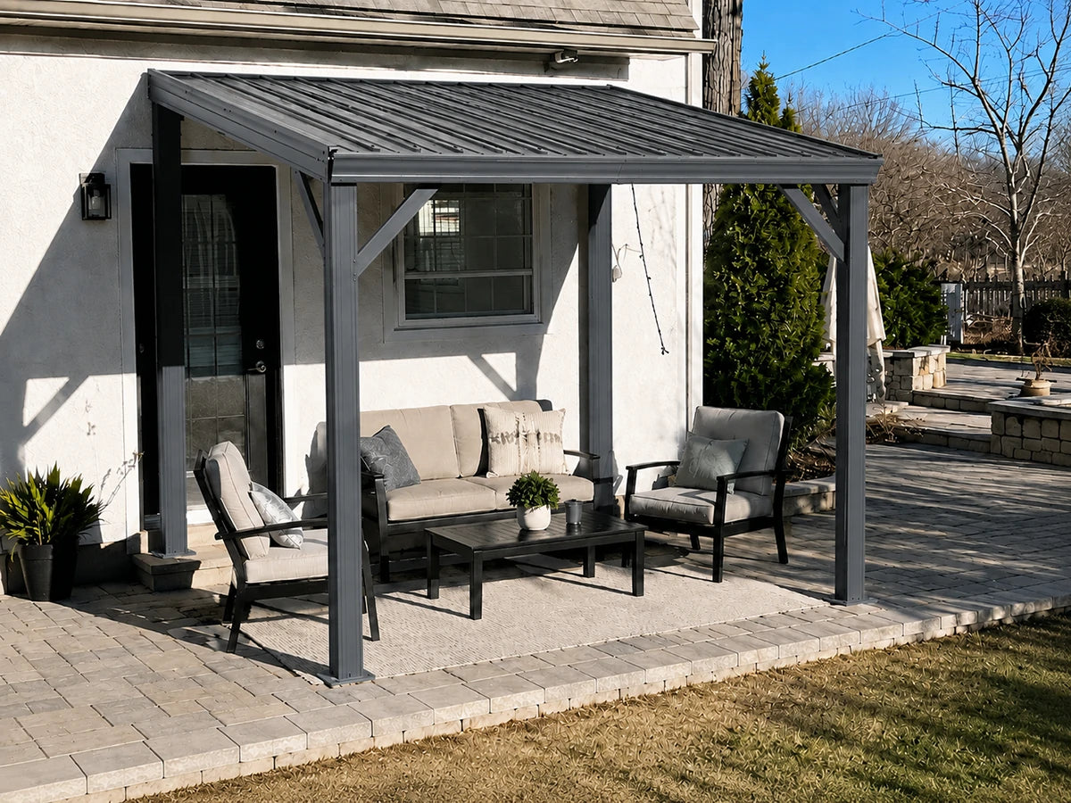 A dark gray metal patio cover with a matching outdoor seating set on a paved backyard patio in front of a white stucco house.