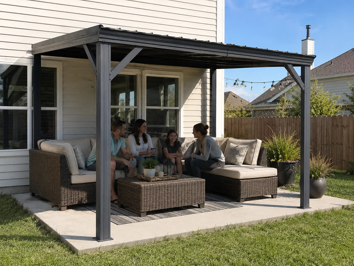 A dark gray metal patio cover with wicker furniture and four people sitting underneath on a concrete patio in a backyard setting.