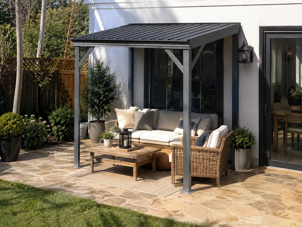 A modern gray metal patio gazebo with a slatted roof, sheltering an outdoor patio set with a wicker sofa, matching armchair, and coffee table on a stone patio.